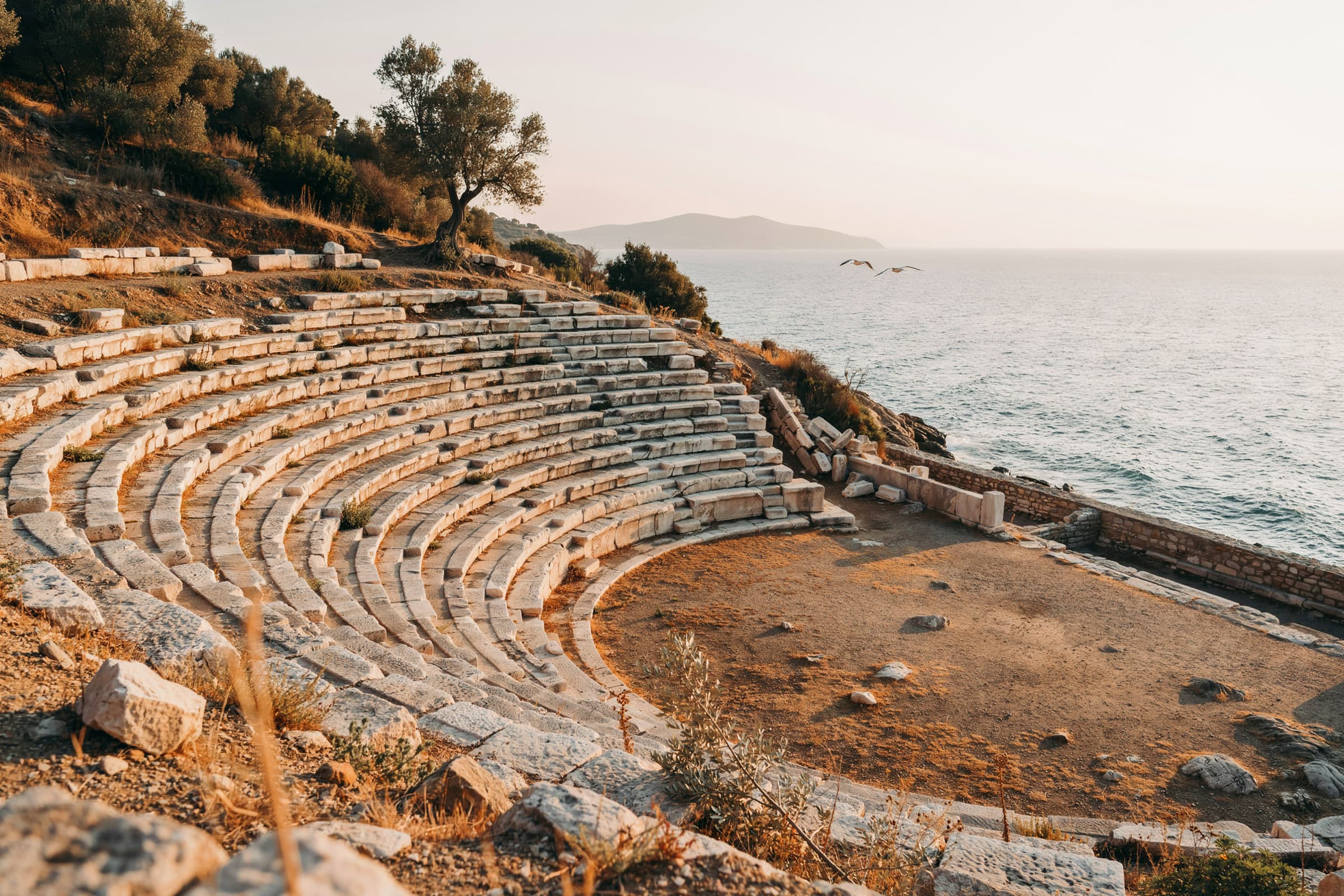 An old stone theater on a hillside above the sea at golden hour.