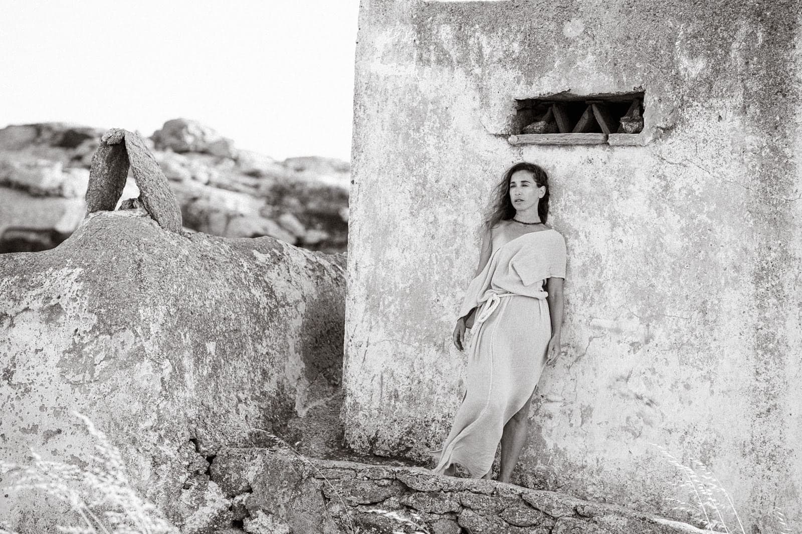 Leaning against a sunlit stone wall among the rocks, in black and white.