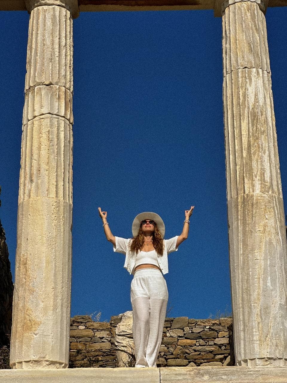 Arms raised between two old stone columns under a deep blue sky.